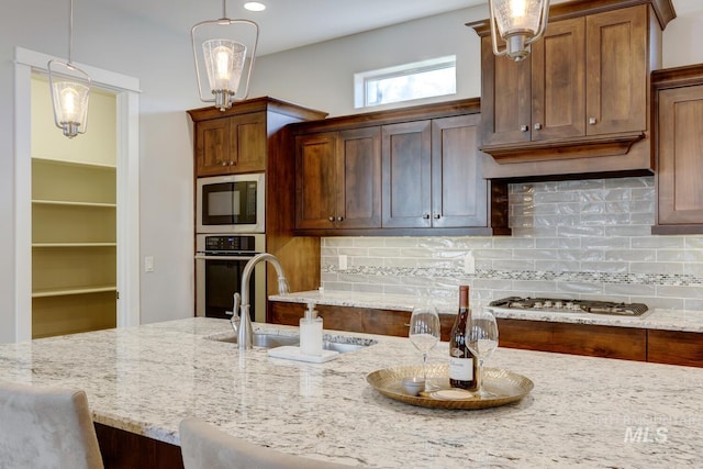 kitchen featuring sink, a breakfast bar area, appliances with stainless steel finishes, light stone countertops, and decorative light fixtures