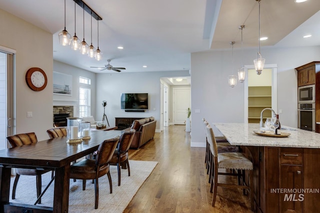 dining space with a stone fireplace, sink, hardwood / wood-style floors, and ceiling fan