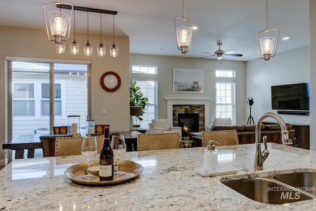 kitchen featuring hanging light fixtures, light stone countertops, sink, and a fireplace