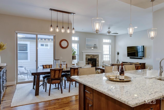 kitchen featuring dark hardwood / wood-style floors, a stone fireplace, an island with sink, and hanging light fixtures