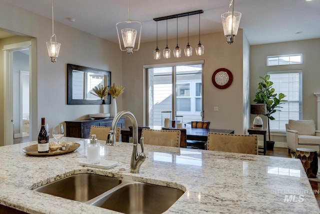 kitchen with hanging light fixtures, an island with sink, light stone countertops, and sink