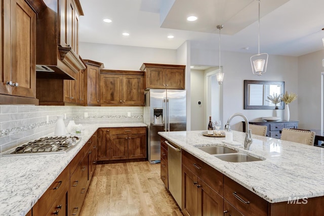 kitchen with sink, light stone counters, hanging light fixtures, a center island with sink, and appliances with stainless steel finishes