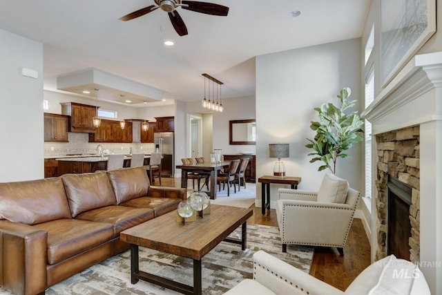 living room with sink, ceiling fan, a wealth of natural light, a stone fireplace, and light wood-type flooring