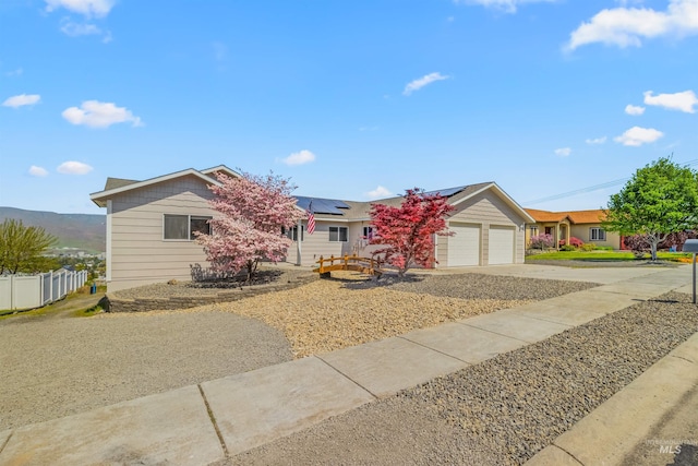 ranch-style house featuring concrete driveway, an attached garage, fence, and roof mounted solar panels