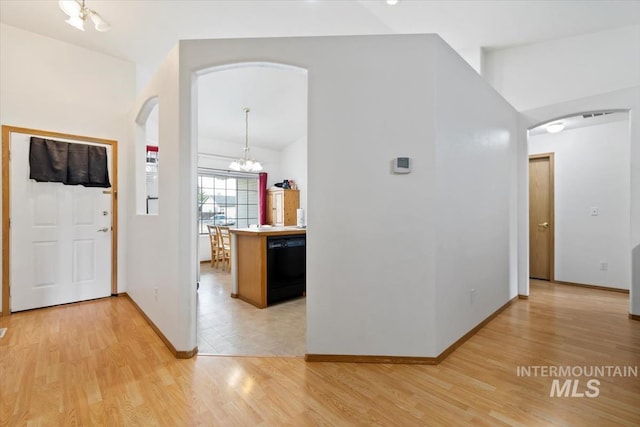 corridor featuring light wood-type flooring, vaulted ceiling, and an inviting chandelier