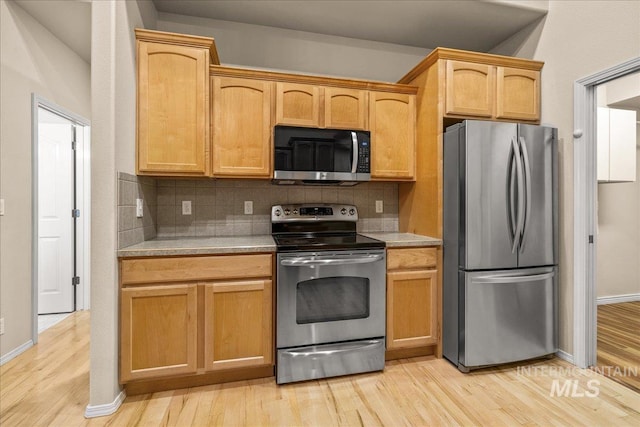 kitchen featuring appliances with stainless steel finishes, light countertops, backsplash, and light wood-style floors