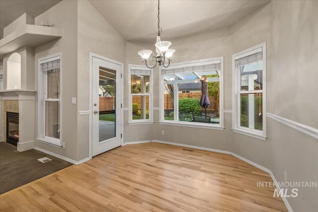 unfurnished dining area with wood finished floors, a chandelier, baseboards, a tile fireplace, and lofted ceiling