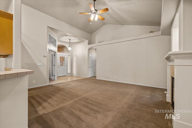 unfurnished living room featuring ceiling fan, carpet flooring, high vaulted ceiling, a glass covered fireplace, and baseboards