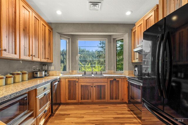 kitchen with black appliances, hanging light fixtures, sink, and light hardwood / wood-style flooring