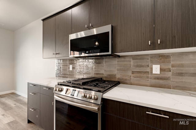 kitchen featuring light wood finished floors, tasteful backsplash, light stone counters, stainless steel appliances, and dark brown cabinets