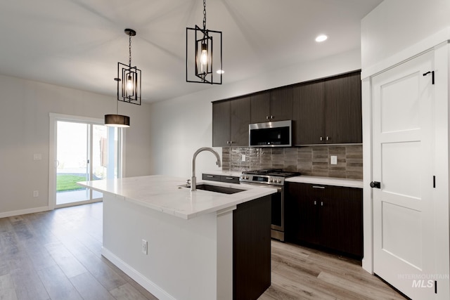 kitchen with decorative light fixtures, backsplash, appliances with stainless steel finishes, light wood-style floors, and a sink