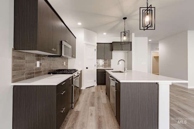 kitchen featuring pendant lighting, stainless steel appliances, light countertops, light wood-style floors, and a sink