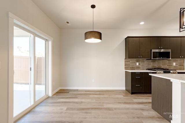 kitchen featuring dark brown cabinetry, a healthy amount of sunlight, light countertops, tasteful backsplash, and stainless steel microwave