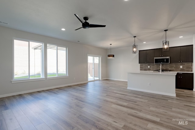 kitchen featuring open floor plan, light countertops, stainless steel microwave, and decorative backsplash