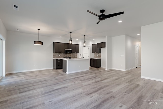 interior space featuring open floor plan, stainless steel microwave, backsplash, and light wood-style floors