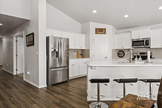 kitchen with white cabinets, lofted ceiling, dark wood-style floors, appliances with stainless steel finishes, and light countertops