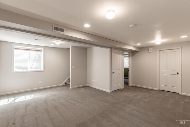 below grade area featuring visible vents, plenty of natural light, dark carpet, and stairway