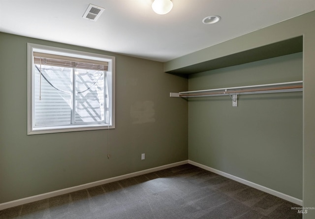 unfurnished bedroom with baseboards, visible vents, dark carpet, and a closet