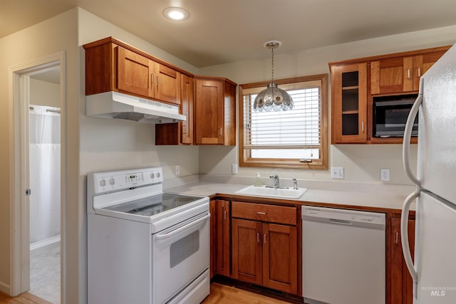 kitchen with white appliances, under cabinet range hood, brown cabinetry, and a sink