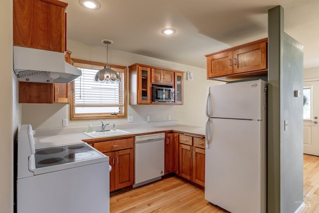 kitchen with brown cabinets, light wood-type flooring, a sink, under cabinet range hood, and white appliances
