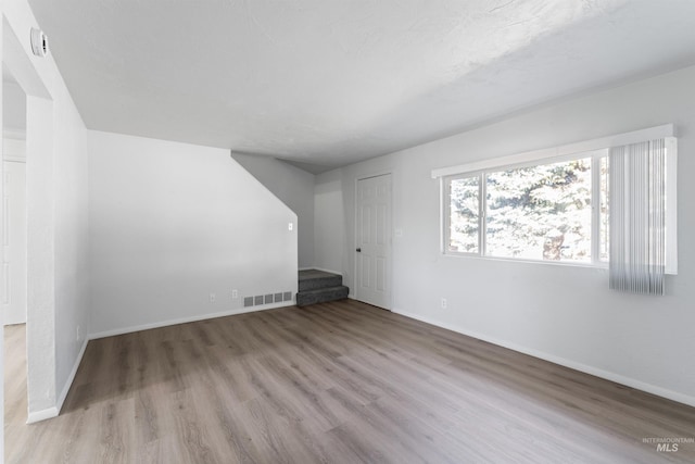 additional living space featuring stairway, baseboards, visible vents, and wood finished floors