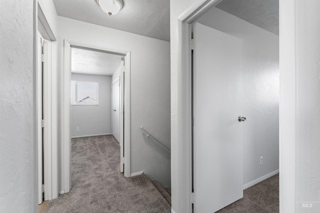 hall with carpet flooring, a textured wall, and an upstairs landing