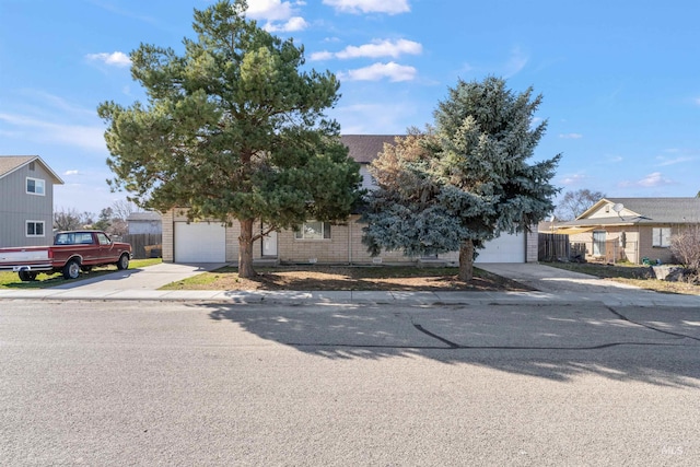 view of property hidden behind natural elements with a garage, driveway, brick siding, and fence