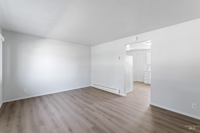 empty room with baseboards, baseboard heating, and wood finished floors