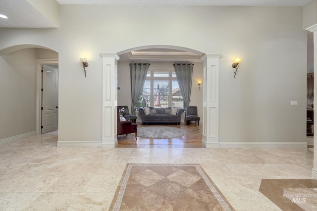 hall with arched walkways, inlaid floor details, baseboards, and ornate columns