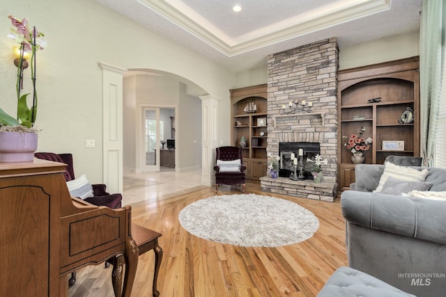 living area with arched walkways, a stone fireplace, decorative columns, a textured ceiling, and wood finished floors