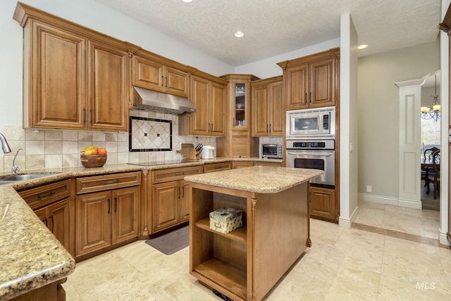 kitchen featuring appliances with stainless steel finishes, under cabinet range hood, a sink, brown cabinets, and recessed lighting