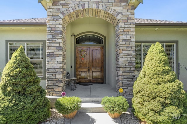 view of exterior entry featuring stucco siding, stone siding, and a shingled roof