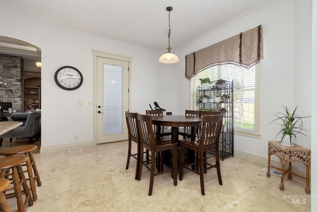dining space with arched walkways, baseboards, and a stone fireplace