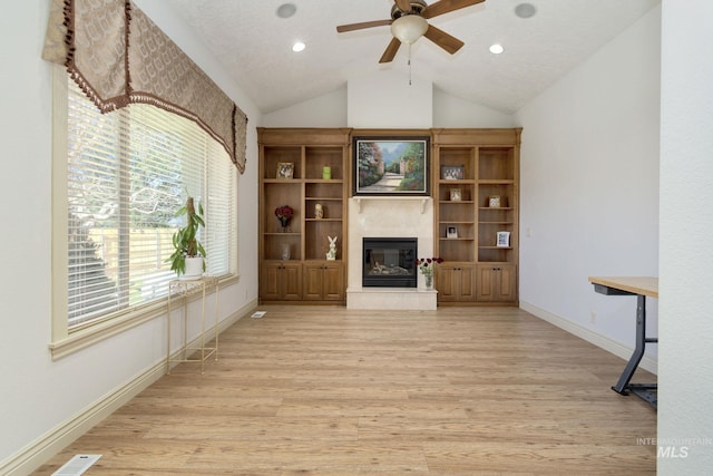 unfurnished living room with light wood-style flooring, a ceiling fan, a glass covered fireplace, baseboards, and vaulted ceiling