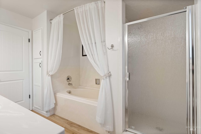 bathroom featuring a stall shower, a tub, and wood finished floors