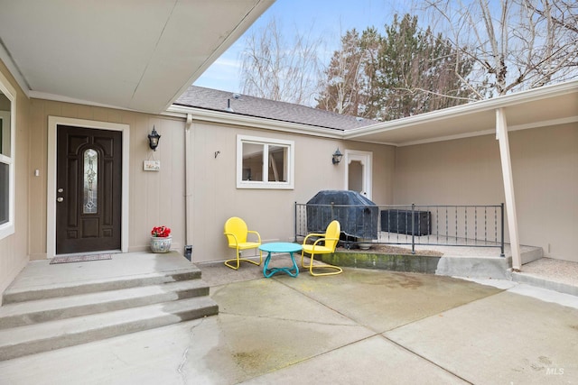 view of exterior entry with a patio area and a shingled roof