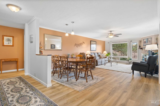 dining room featuring a ceiling fan, baseboards, light wood-style floors, ornamental molding, and a glass covered fireplace