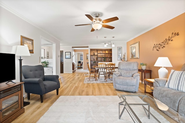 living area with ornamental molding, light wood finished floors, and a ceiling fan