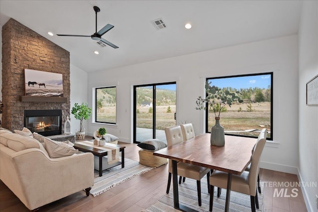 dining room with visible vents, a large fireplace, ceiling fan, vaulted ceiling, and wood finished floors