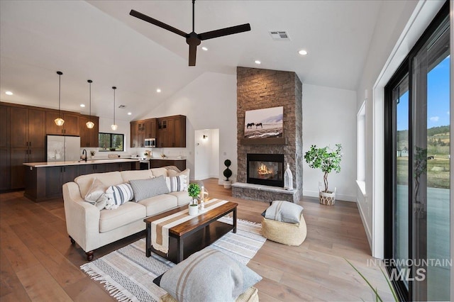 living room with high vaulted ceiling, visible vents, wood finished floors, and a stone fireplace