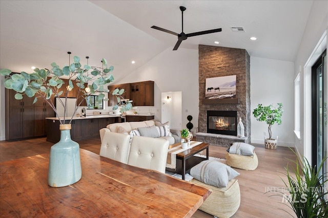 living room featuring a fireplace, visible vents, a ceiling fan, wood finished floors, and high vaulted ceiling