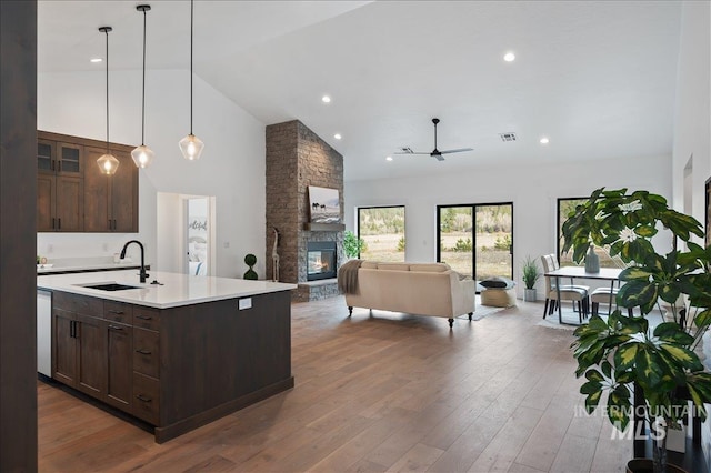 kitchen with dark brown cabinetry, light countertops, a sink, and a stone fireplace