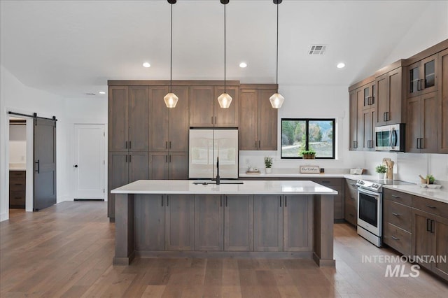 kitchen with light countertops, visible vents, a barn door, appliances with stainless steel finishes, and a kitchen island with sink