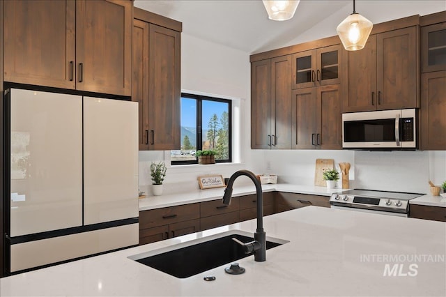 kitchen featuring decorative light fixtures, lofted ceiling, appliances with stainless steel finishes, glass insert cabinets, and a sink