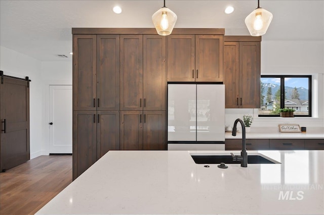 kitchen with a barn door, wood finished floors, freestanding refrigerator, hanging light fixtures, and a sink