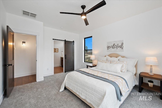 carpeted bedroom featuring ceiling fan, ensuite bathroom, a barn door, visible vents, and baseboards