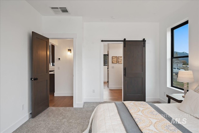 bedroom featuring carpet, a barn door, visible vents, and baseboards