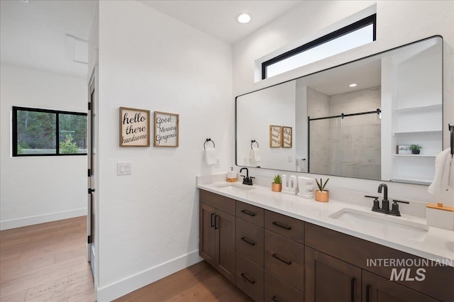 full bathroom featuring double vanity, wood finished floors, a stall shower, and a sink