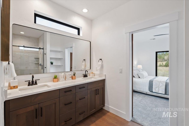 ensuite bathroom with double vanity, a stall shower, a sink, and wood finished floors