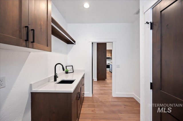 kitchen featuring a sink, dark brown cabinets, light countertops, light wood-type flooring, and stainless steel microwave